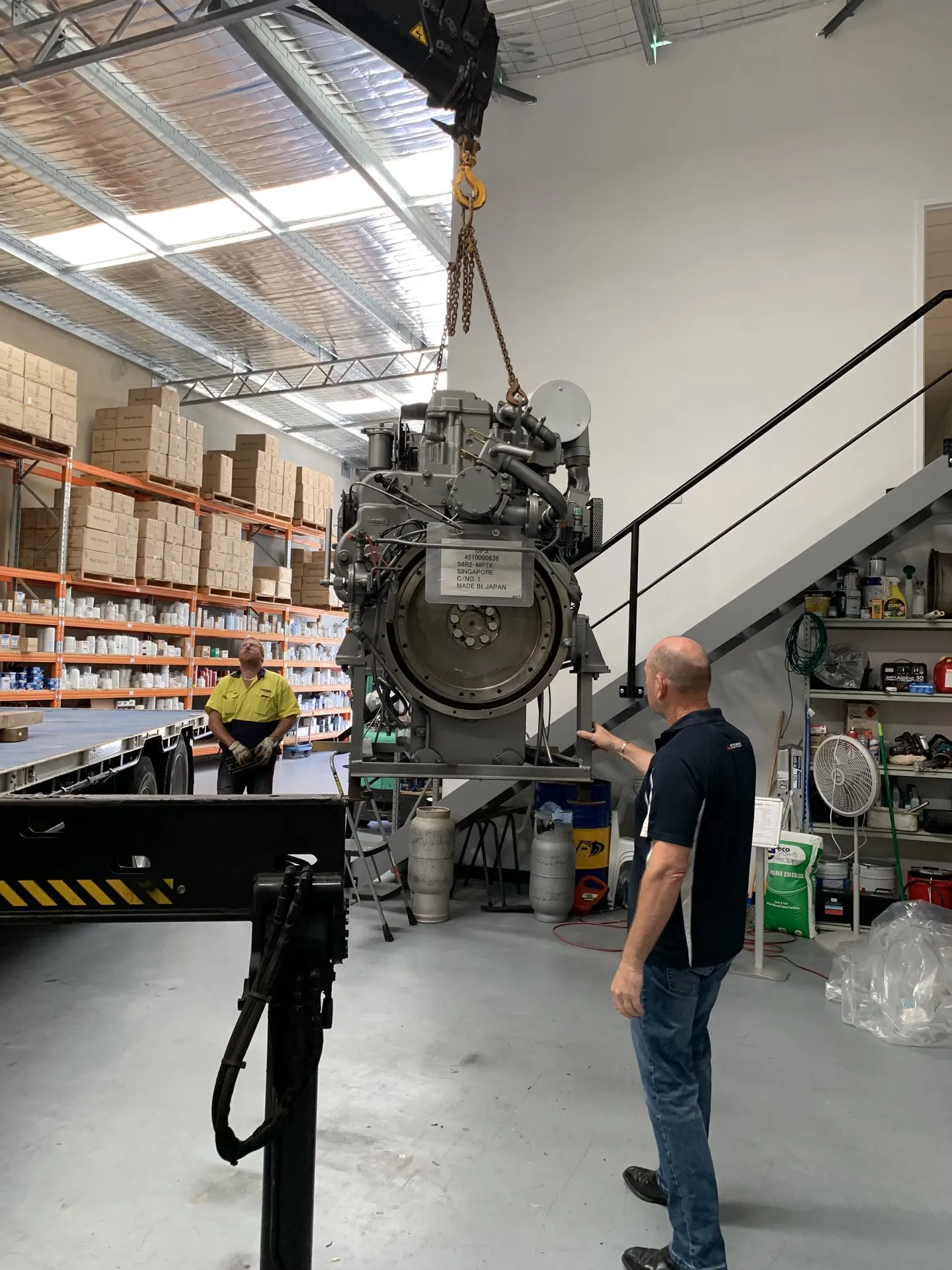 An S6R2-MPTK marine engine being craned off a delivery truck at OPS's Wangara warehouse, with two staff members guiding the lift