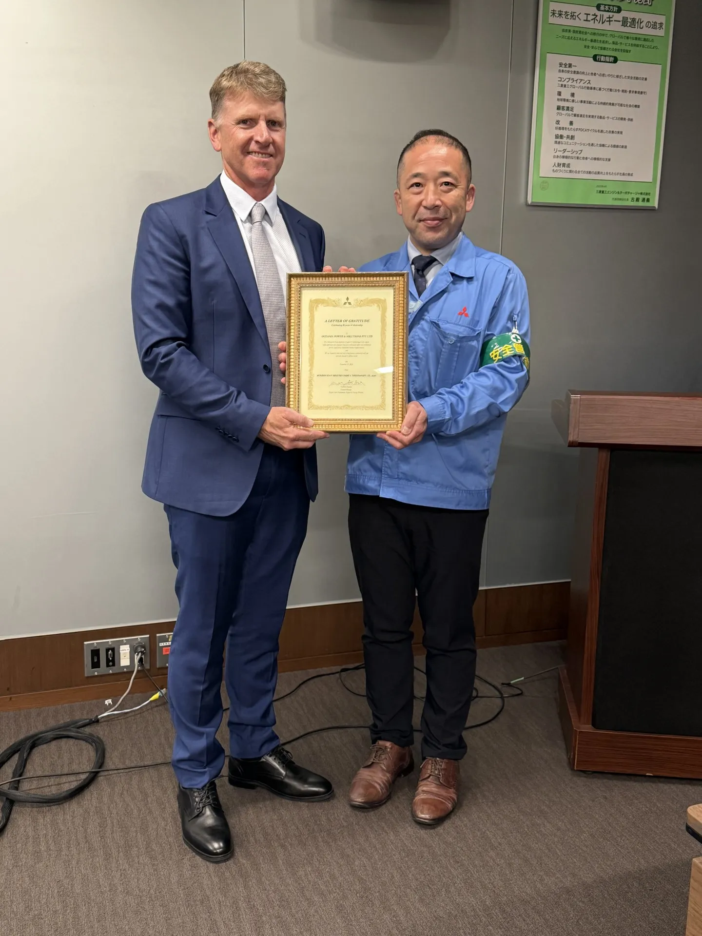 An OPS representative and an MHI representative in Japan holding a framed Letter of Gratitude marking 10 years of dealership